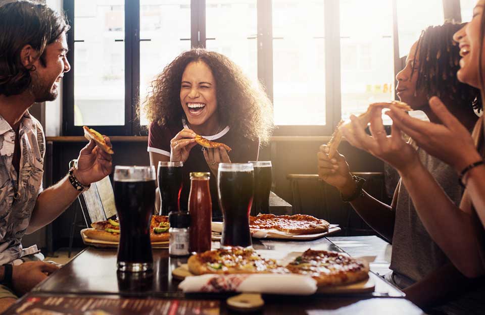A group of friends laughing over pizza and drinks.