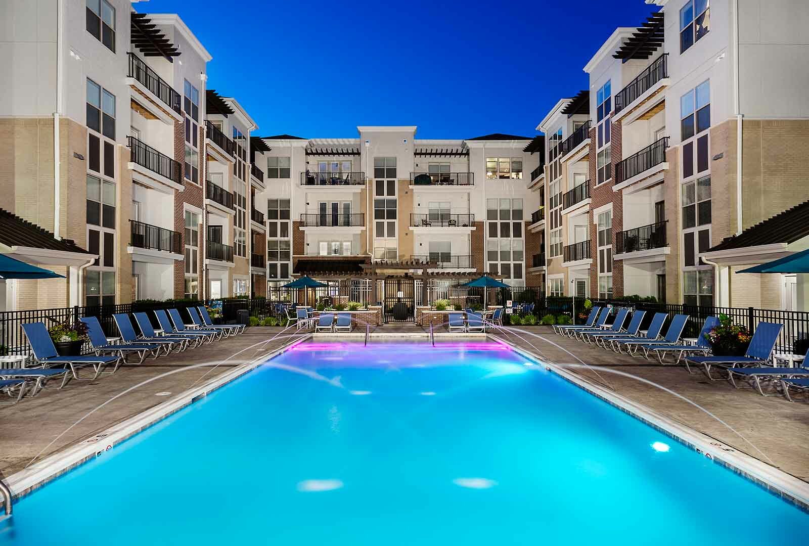 Luxury swimming pool lit up at night with water features and underwater lights.