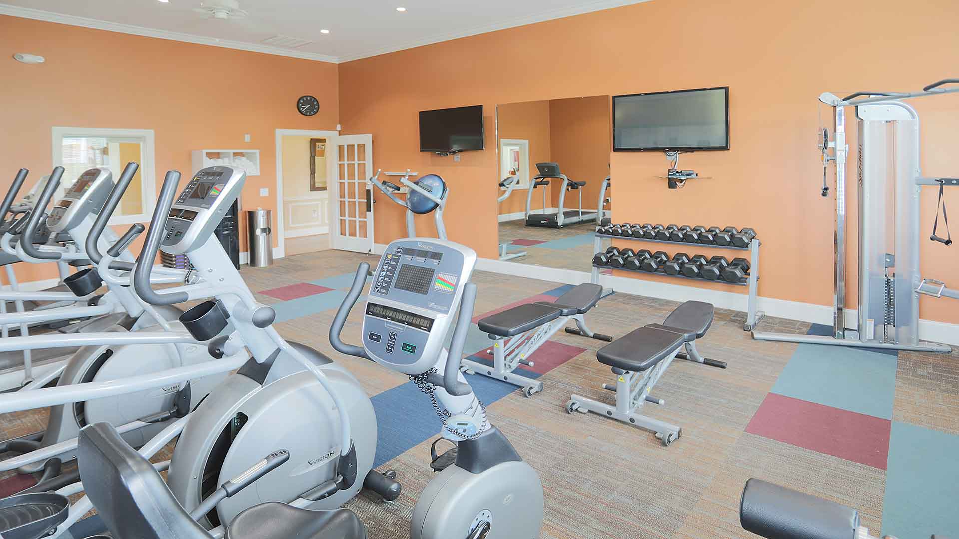 Fitness room with cardio machines and dumbbells.