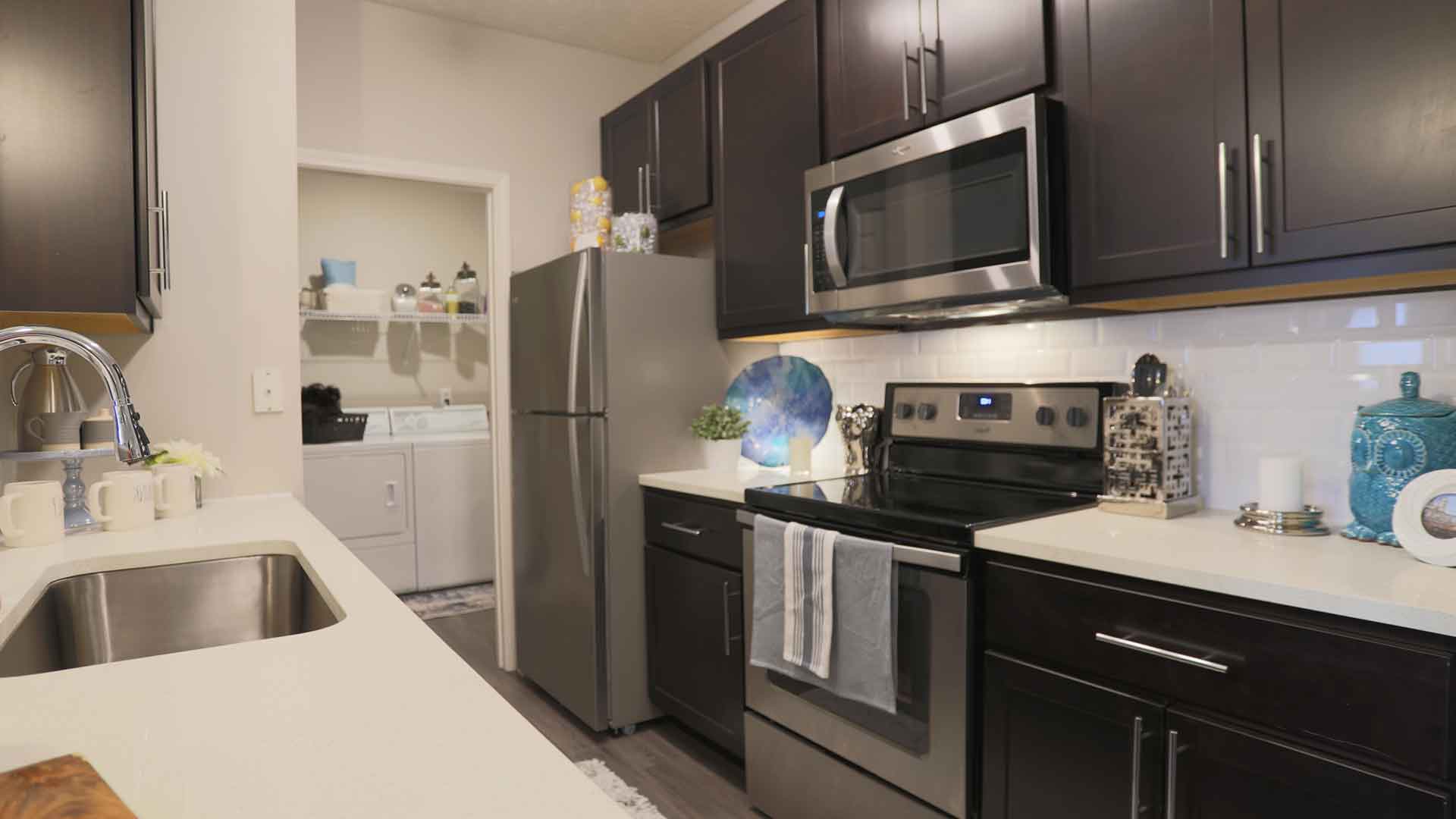 Apartment kitchen with stainless steel appliances and dark wood cabinets.