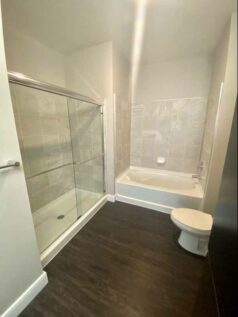 Apartment bathroom with wood grain flooring, a sliding-door shower, and a bathtub.