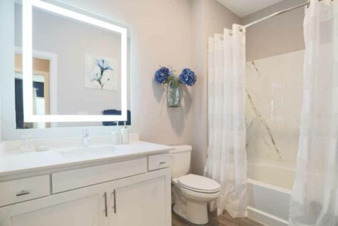 Bathroom with lit mirror and bathtub with a curved shower rod.