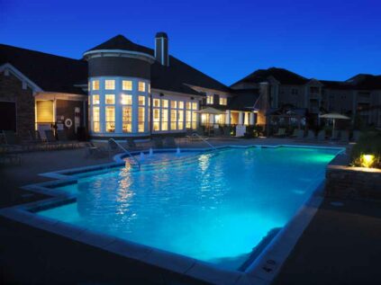 Beautiful pool area next to clubhouse with lounge chairs lit at night.