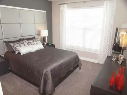 Large apartment bedroom with carpet flooring and a window.