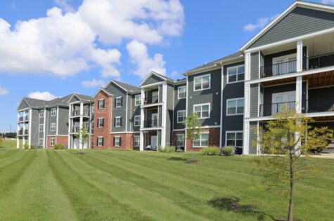 A large, three story apartment building looks out over a well-maintained lawn.
