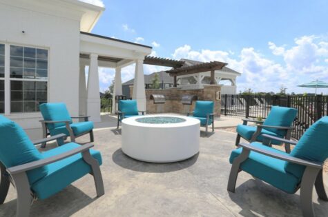 A glass bead fire pit surrounded by outdoor patio chairs next to a clubhouse building.