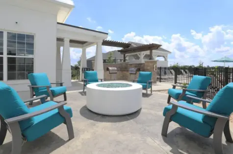 A glass bead fire pit surrounded by outdoor patio chairs next to a clubhouse building.