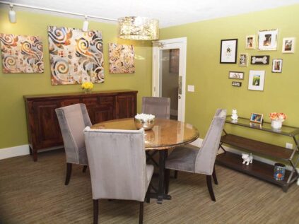 A dining room featuring modern art, a dining table surrounded by chairs, and a small cabinet.