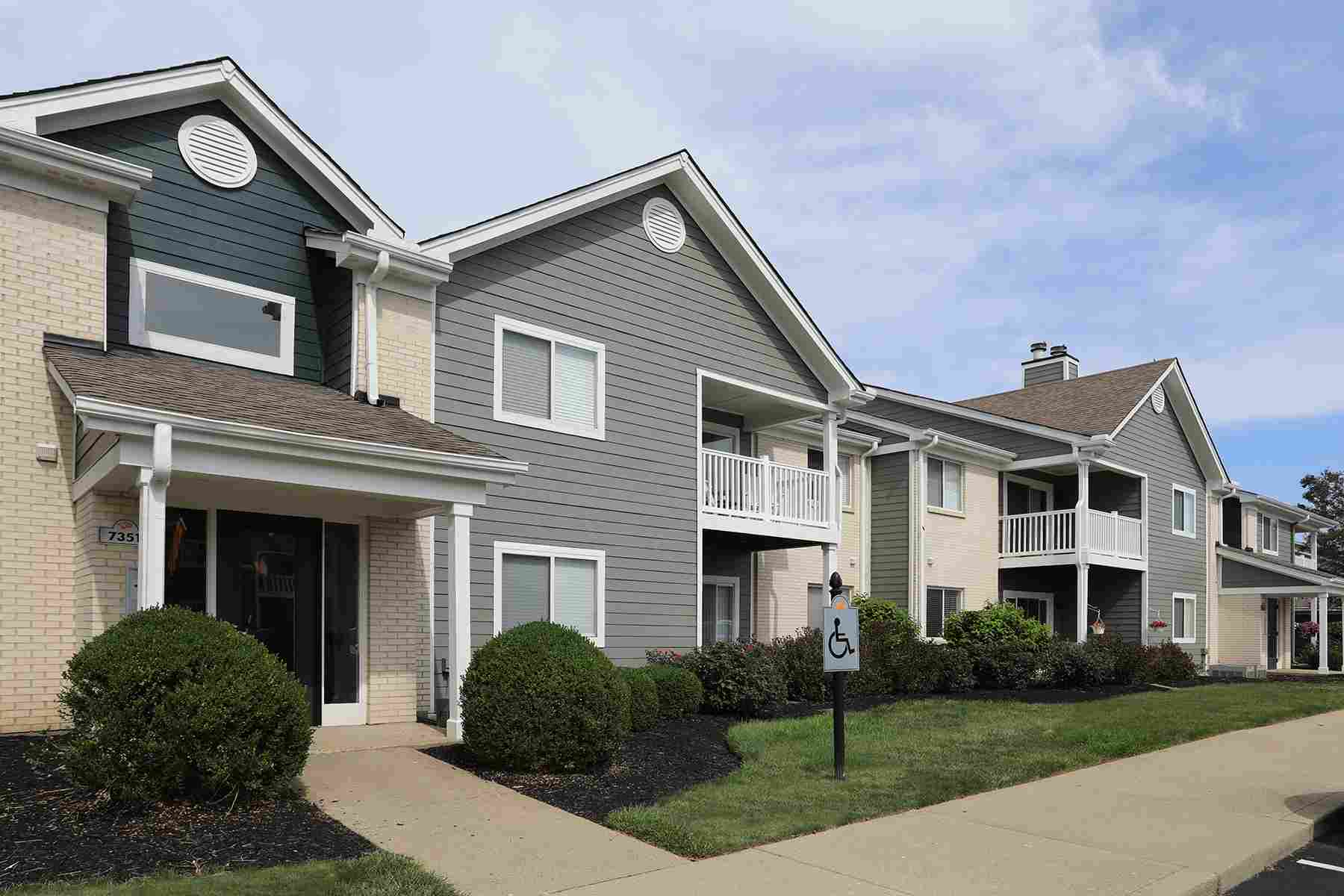 A two story apartment complex overlooks a parking lot featuring handicap accessible parking.