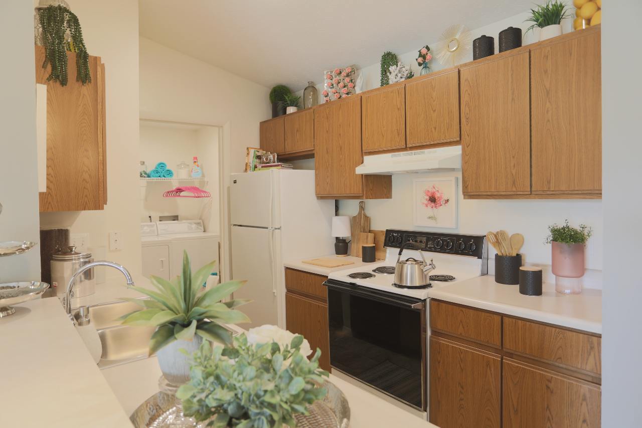 An alley kitchen with dark walnut cabinets and white appliances connected to in-unit laundry room.