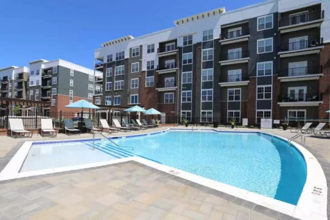 A small clean pool overlooked by a large, modern apartment building.