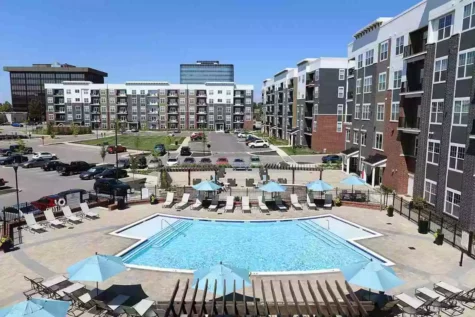 A medium sized pool surrounded by patio chairs, overlooked by large, new apartments.