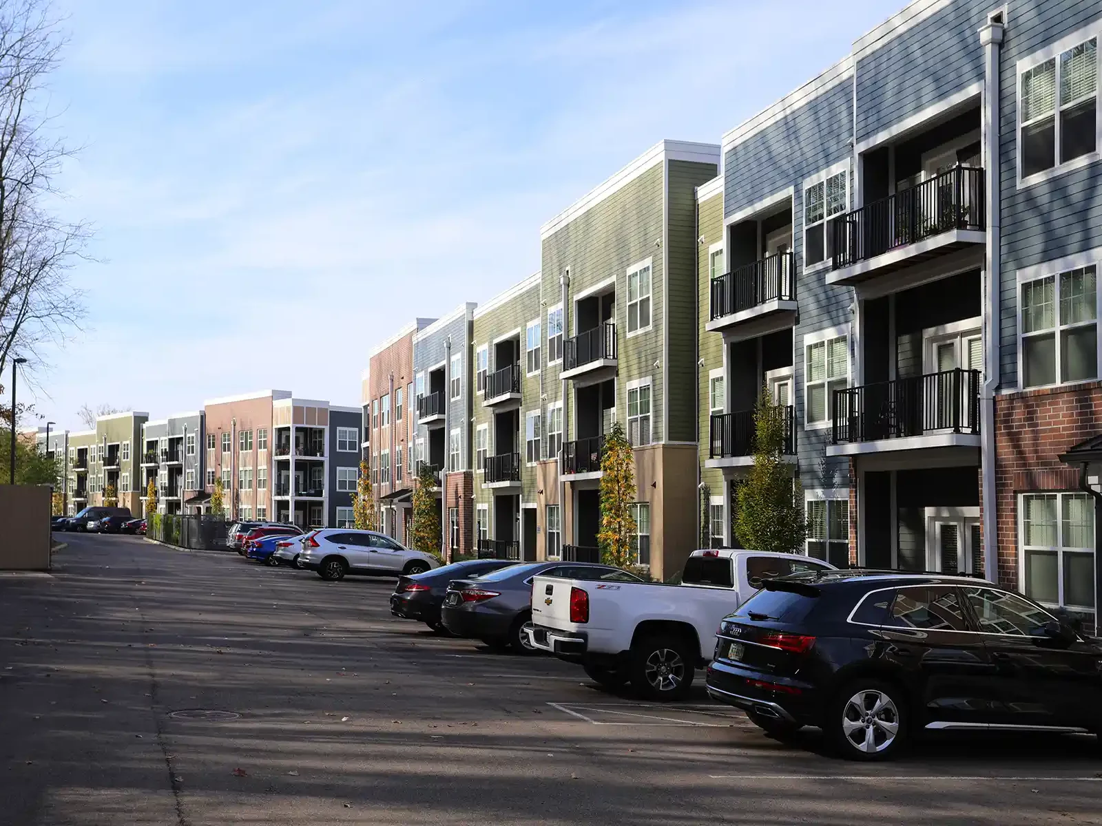A parking lot, moderately filled with cars, outside an apartment building.