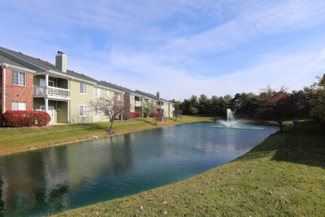 A large pond with a fountain sits behind several apartment buildings.