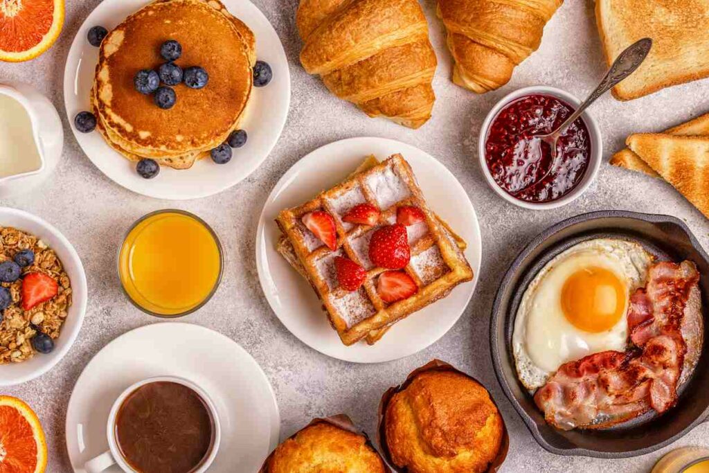 Various breakfast foods placed on a table, including pancakes, waffles, eggs, bacon, and coffee.