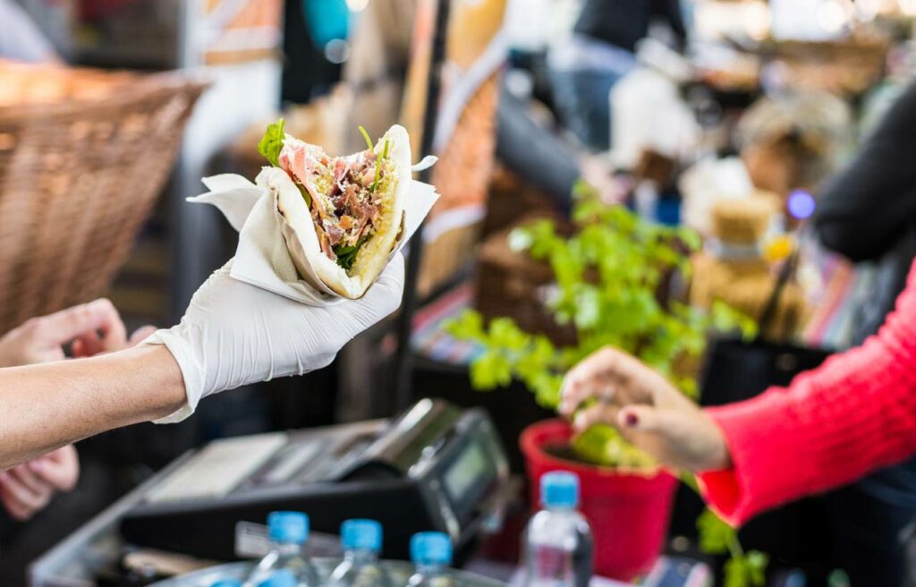 A restaurant vendor serving a gyro sandwich wrapped in wax paper.