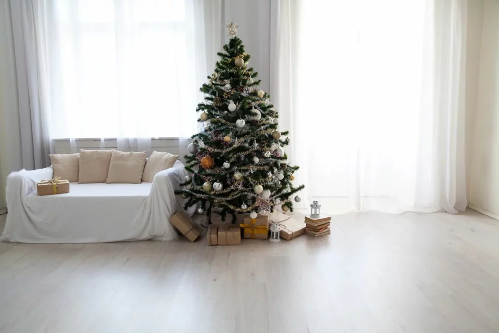 A small Christmas tree is decorated with gold and white accents and presents wrapped in brown paper, set up in a spacious living room.