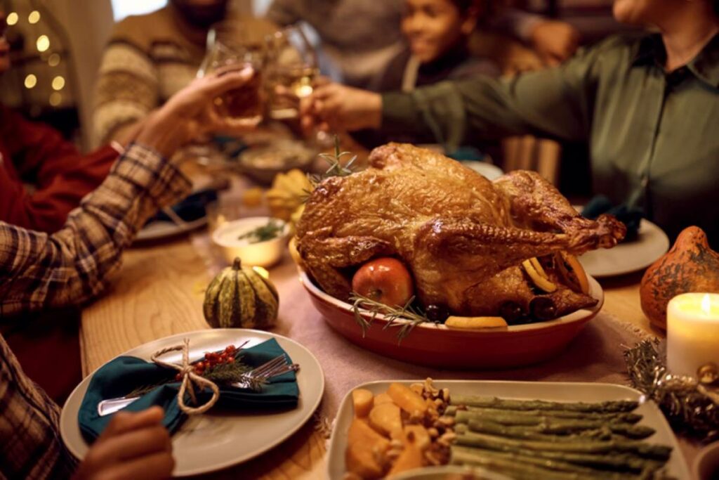 : Friends clinking glasses around a thanksgiving dinner with a turkey and green beans on the table