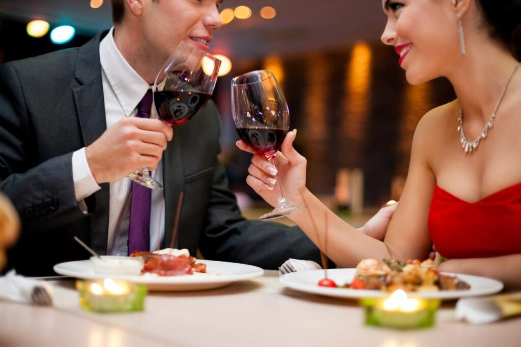 A couple toasts with glasses of red wine while on a date.