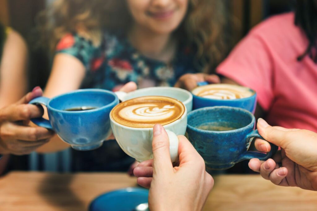 Five friends toast with cups of coffee and lattes while hanging out in a cafe.