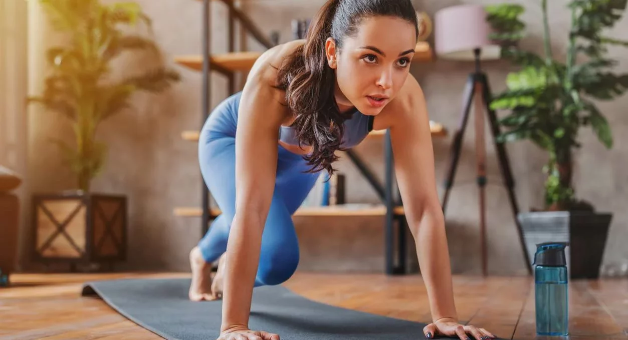 A young woman stretching and exercising indoors on a yoga mat.