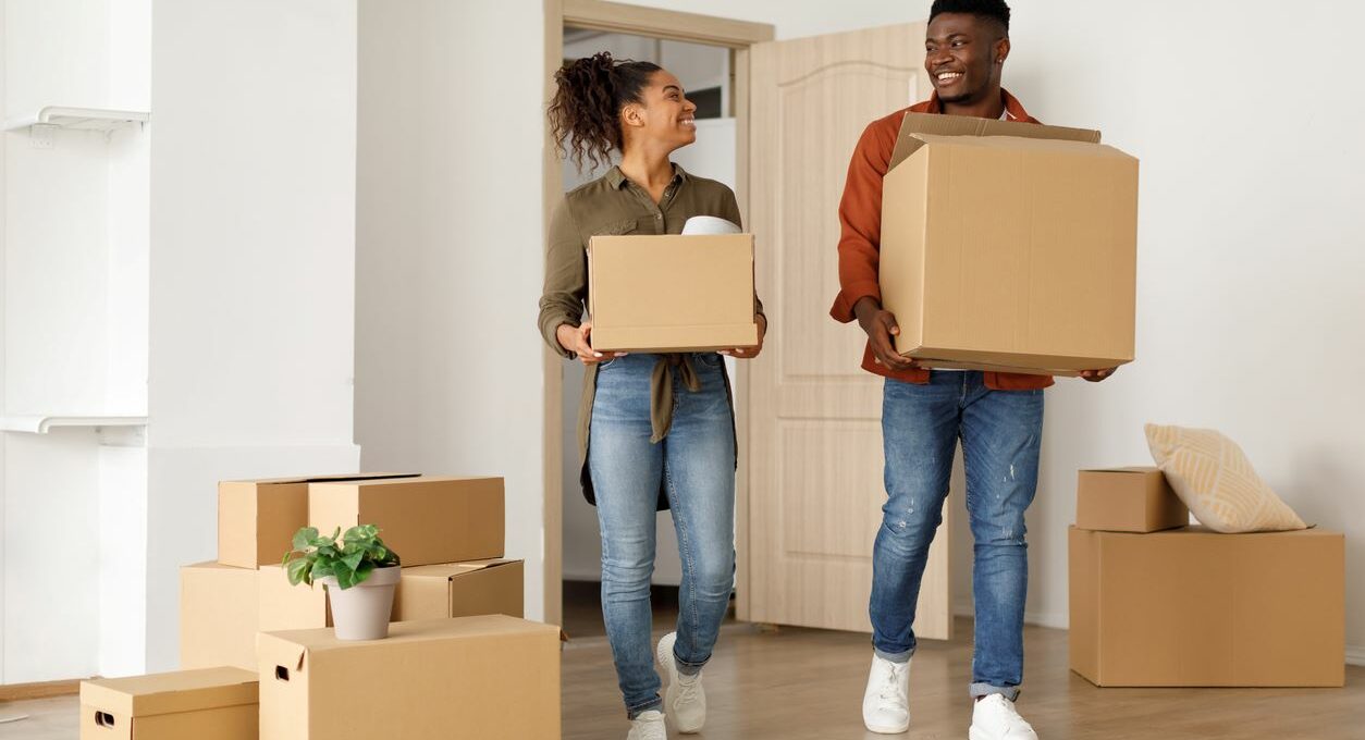 Two smiling young adults carrying boxes on moving day.