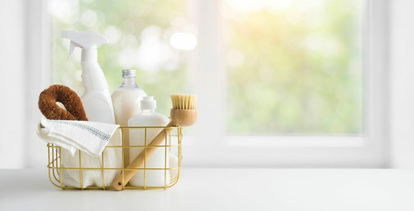 Eco-friendly cleaning products in a basket on a table with a window in the background.