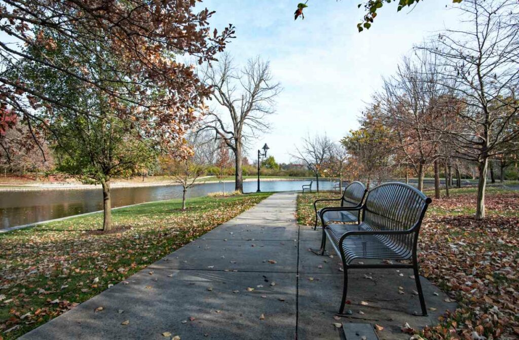 An Ohio park with black wrought iron benches and a sidewalk leading to a pond in late fall.