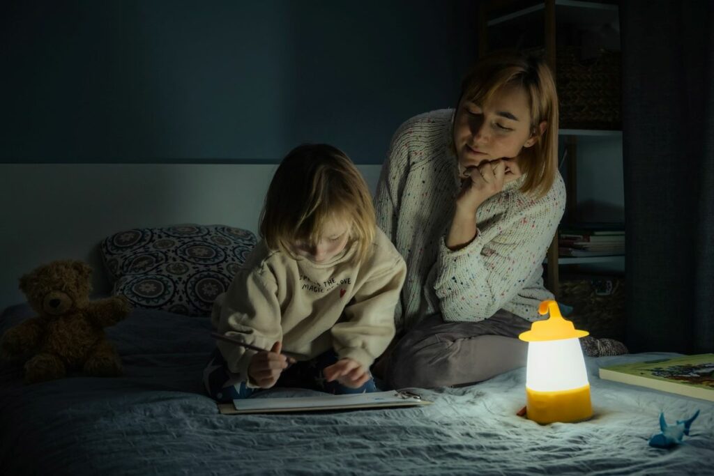 A mother and daughter drawing during a power outage with a lantern lit.