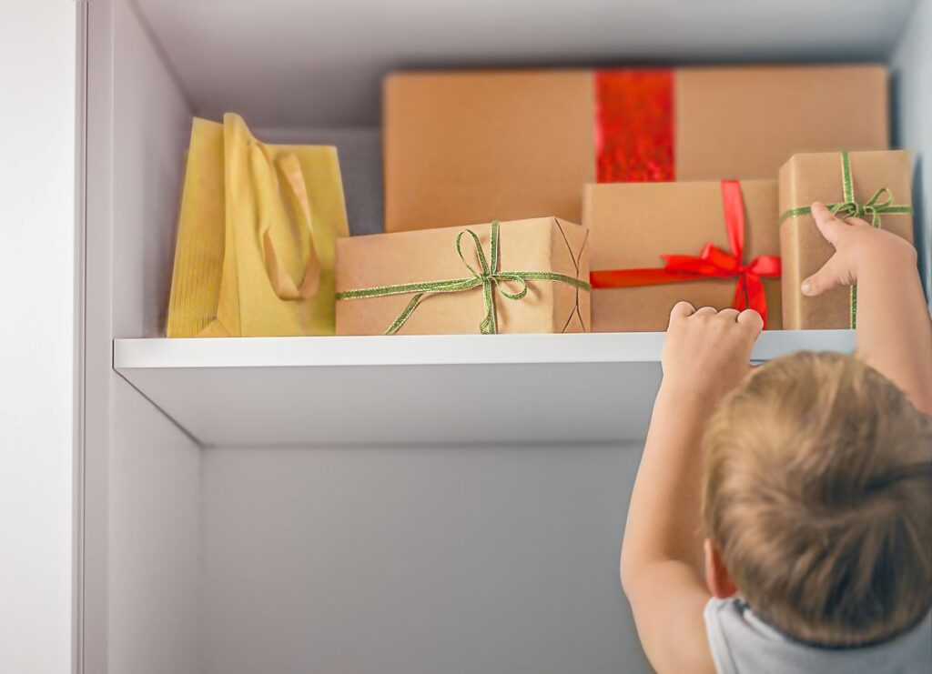 A child reaches for the holiday gifts on the top shelf of a closet.