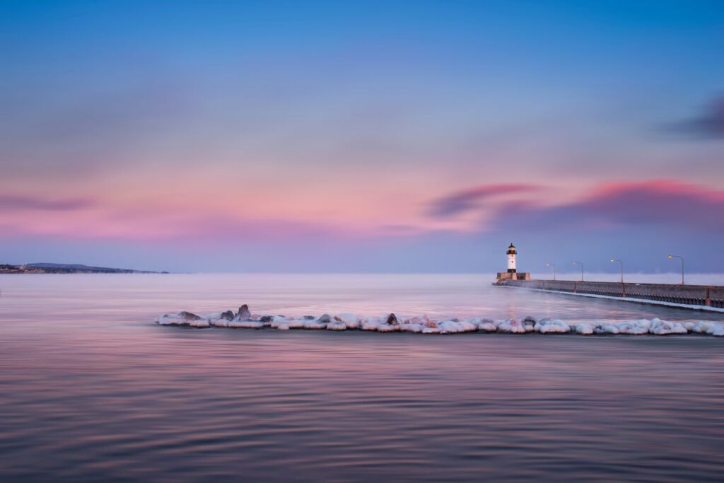 At sunset, a lighthouse on Lake Superior in Duluth, MN, along a snowy pier.