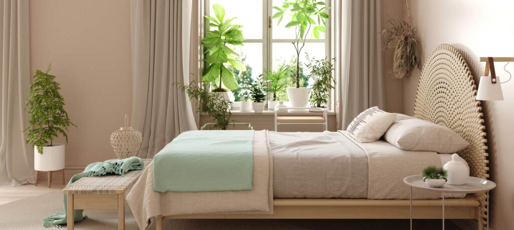 A bed layered with bedding is surrounded by green plants.