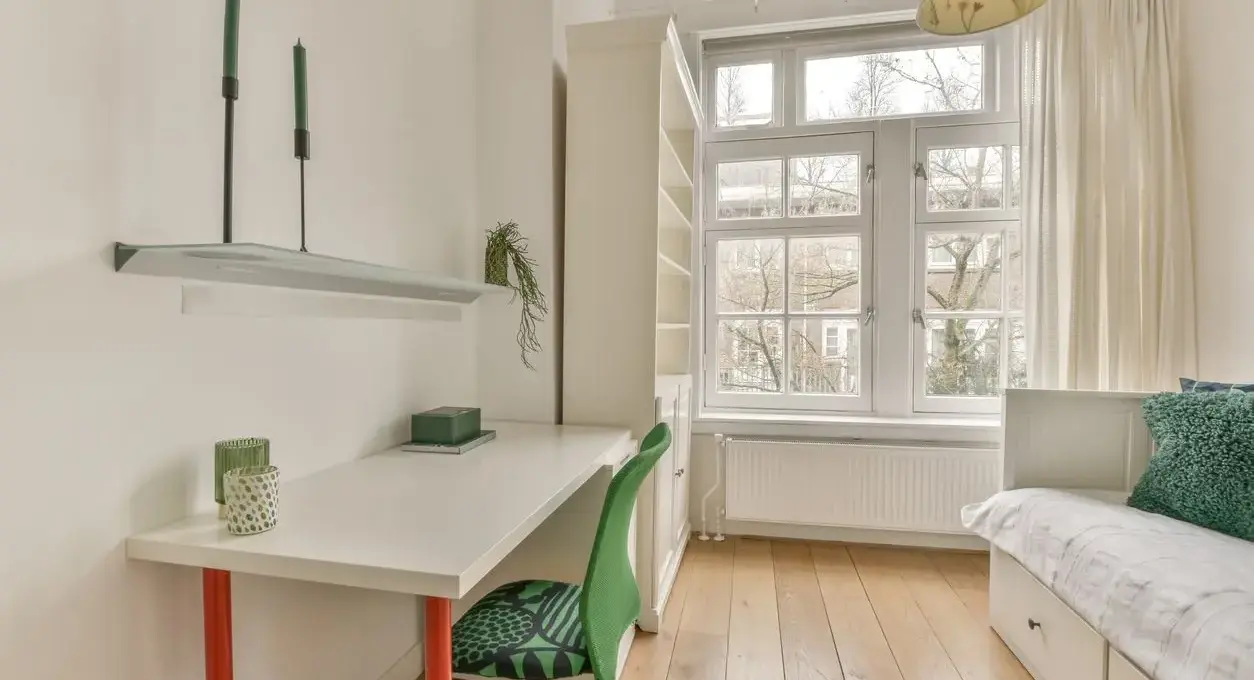 A minimalist spare bedroom with a desk, daybed, bookshelf, and large windows.