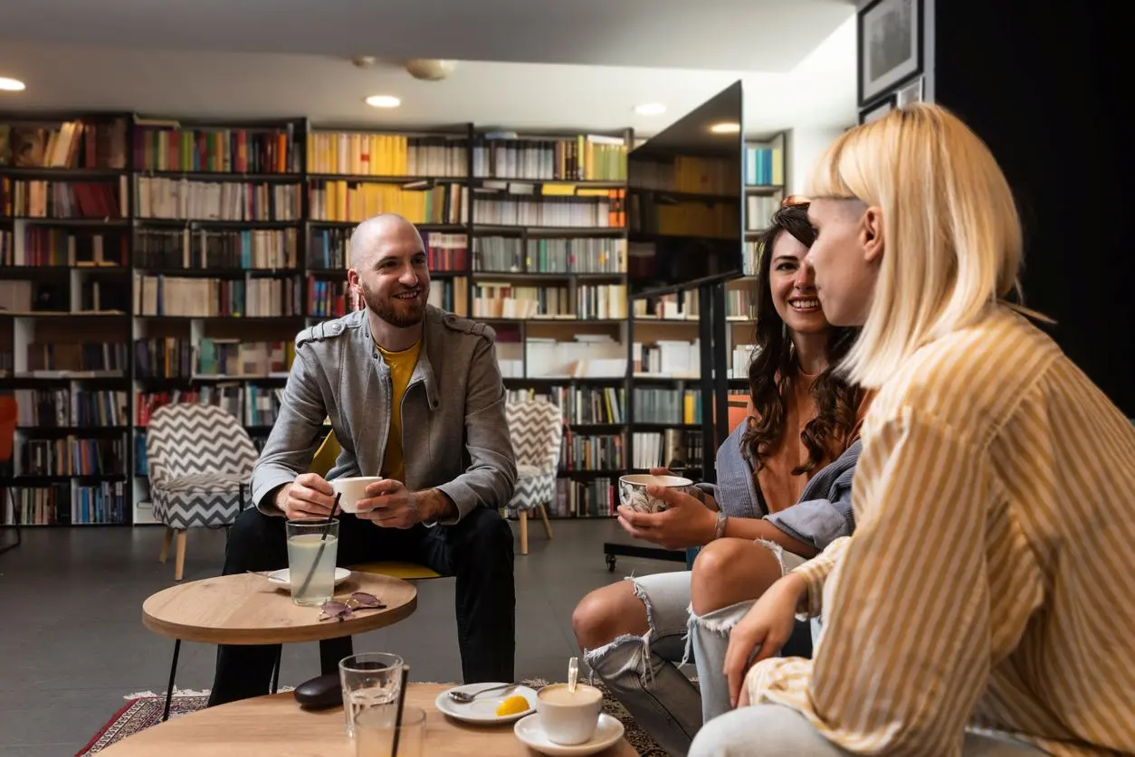 A group of three friends sip on coffee and chat in a library.