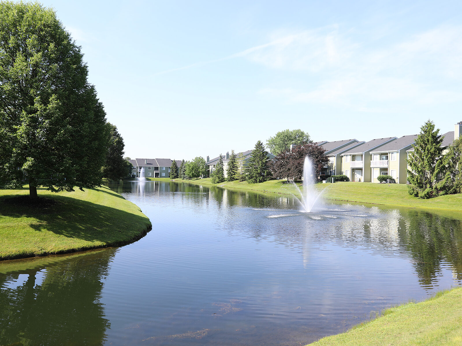 Pond view at Emerald Lakes Apartments in Greenwood, Indiana, overlooking the community with calm water, landscaped surroundings, and apartment buildings in the background.