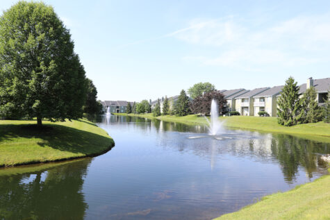 Pond view at Emerald Lakes Apartments in Greenwood, Indiana, overlooking the community with calm water, landscaped surroundings, and apartment buildings in the background.