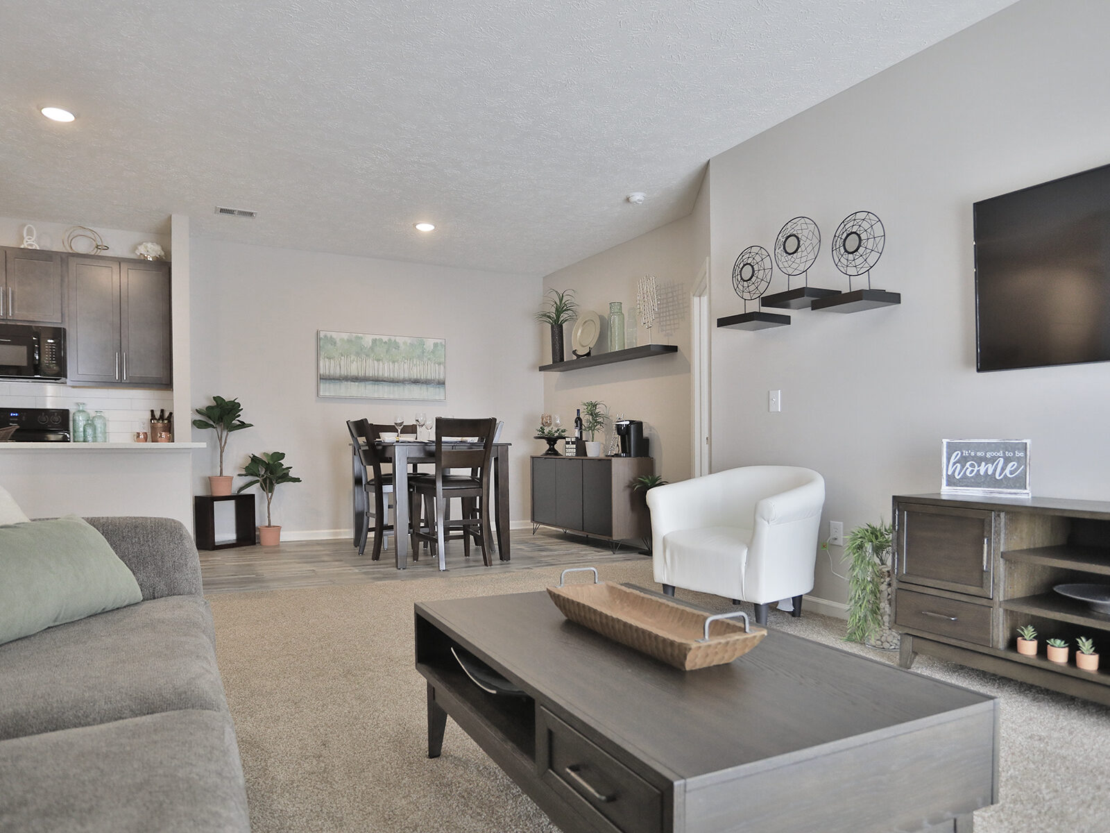 Full model view at Emerald Lakes Apartments from the dining room, showcasing an open-concept layout with sightlines into the living room, kitchen with modern finishes, and guest wing of the home.