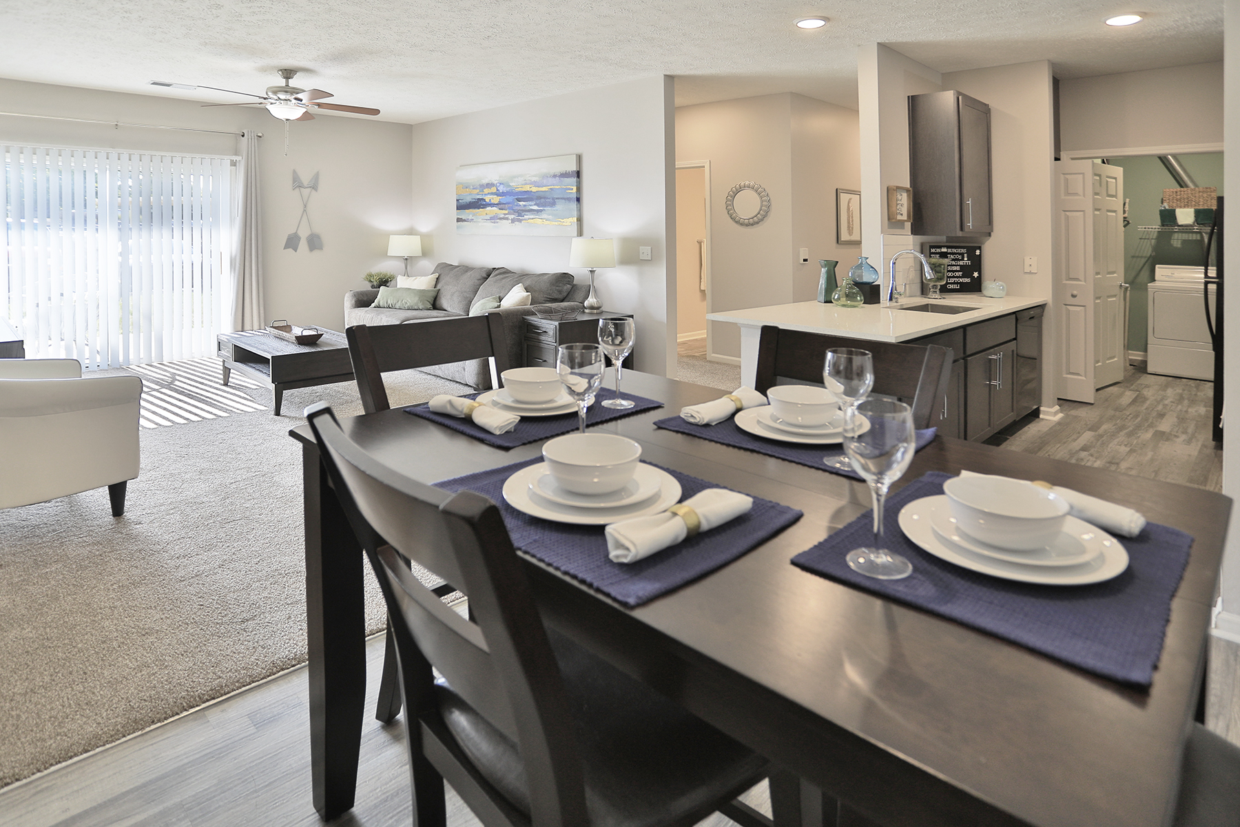 Full model view at Emerald Lakes Apartments from the dining room, showcasing an open-concept layout with sightlines into the living room, kitchen with modern finishes, and guest wing of the home.