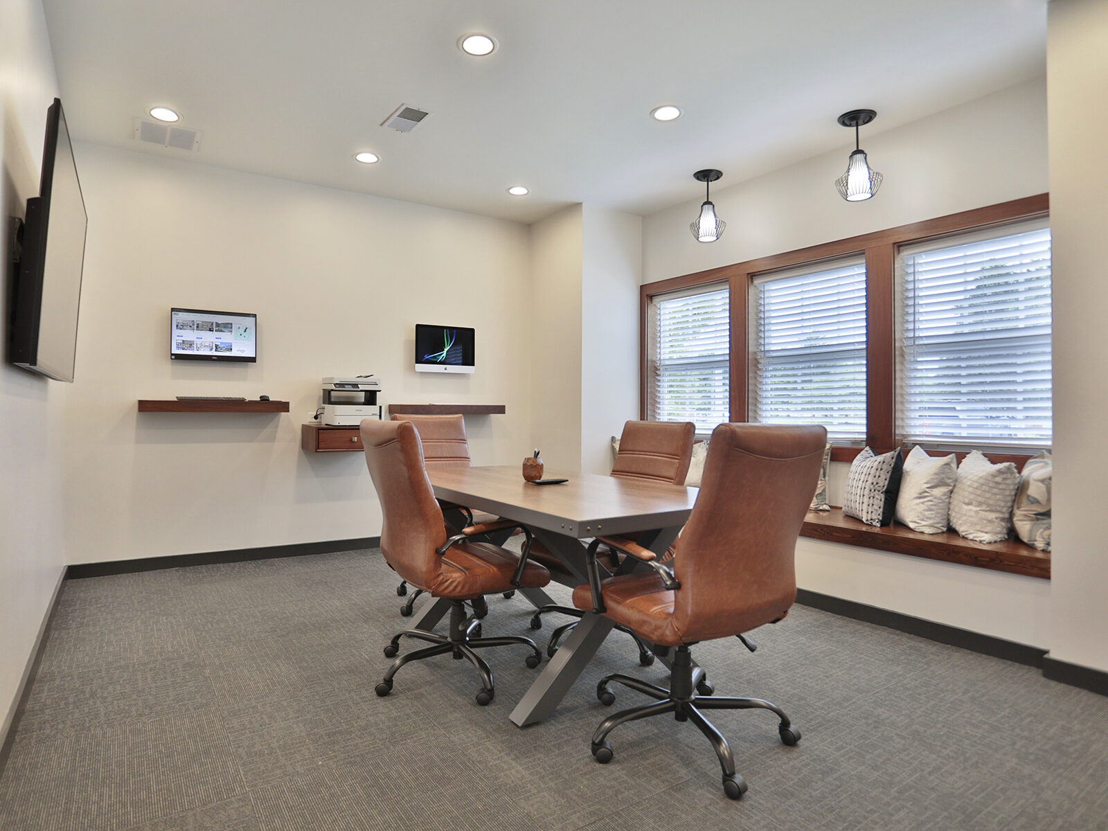 Business center at Wellington Place Apartments featuring Mac and PC workstations, a conference table, wireless printing, and charging stations in a modern, professional setting.