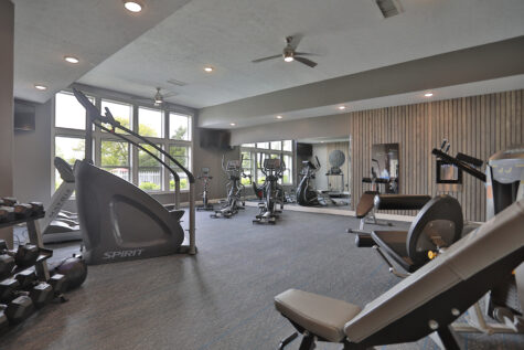 Fitness center at Wellington Place Apartments featuring cardio machines like treadmills and a StairMaster, a Mirror personal trainer, multifunctional weight machines, and free weights in a spacious, modern setting.