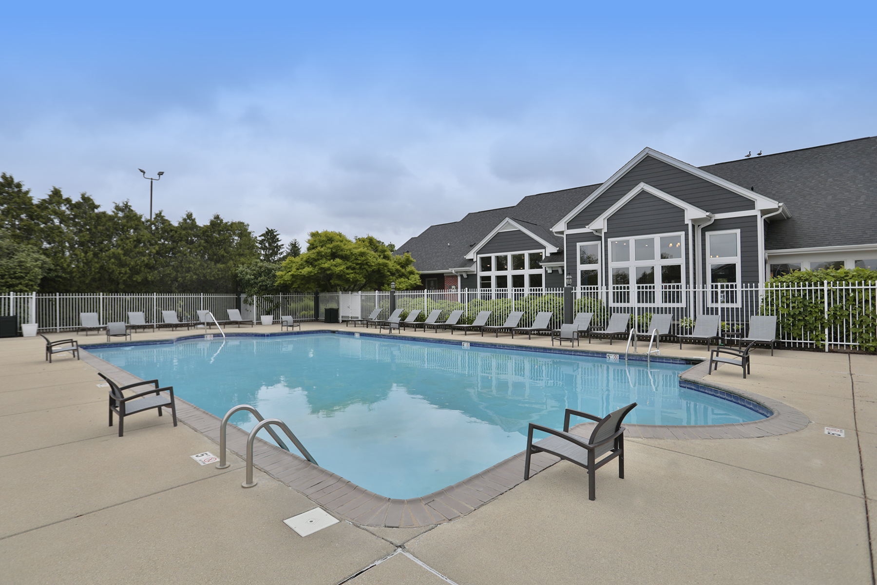 Resort-style swimming pool at Wellington Place Apartments in Fishers, IN, featuring lounge chairs, clear blue water, and a beautifully landscaped setting.