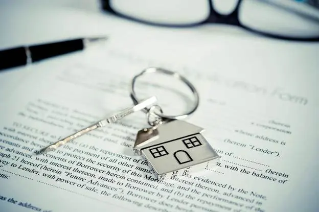 A key on a key ring with a metal charm of a house sits on top of a rental application.