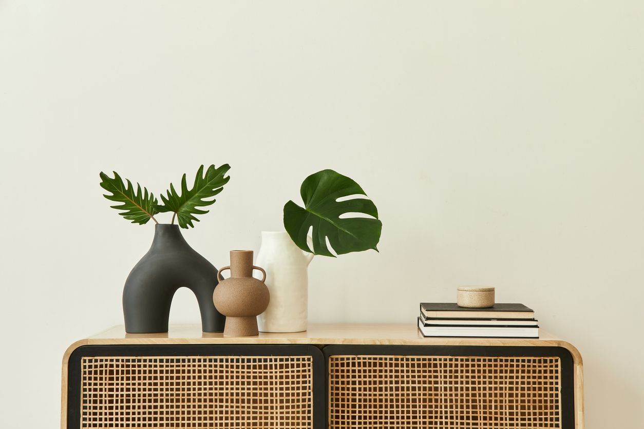 Modern home interior with design wooden commode, tropical leaf in vase, books and personal accessories in stylish home decor.