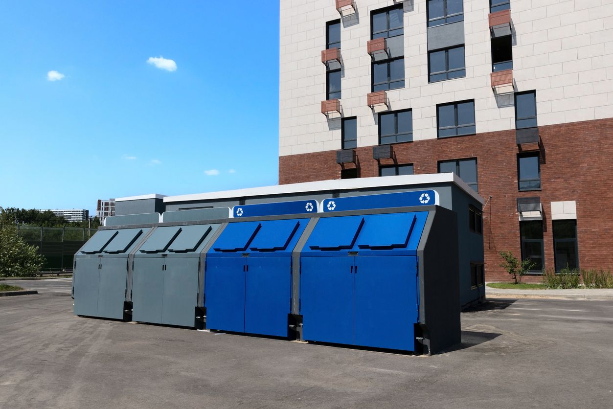 Trash bins and recycling containers outside an apartment building.