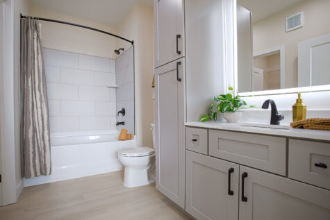 Spacious full bathroom at Relay 129 featuring soaking tub, white quartz counters, LED backlit mirror, matte black fixtures, and grey cabinetry.