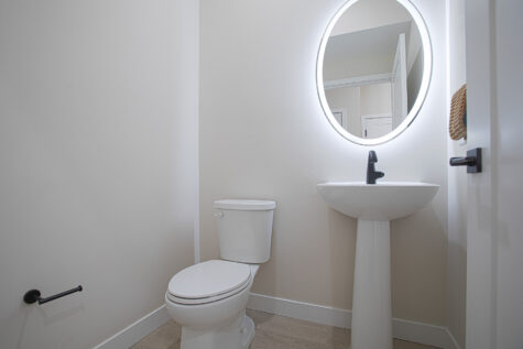 Contemporary half bathroom at Relay 129 featuring white quartz vanity, matte black hardware, modern lighting, and sleek cabinetry.