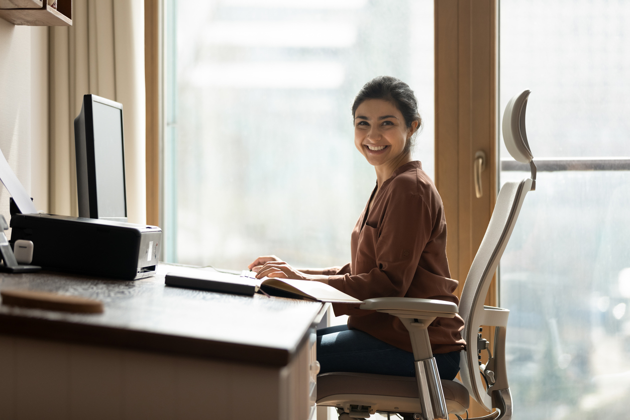 A woman sits in an ergonomic desk chair while working from home in her apartment.