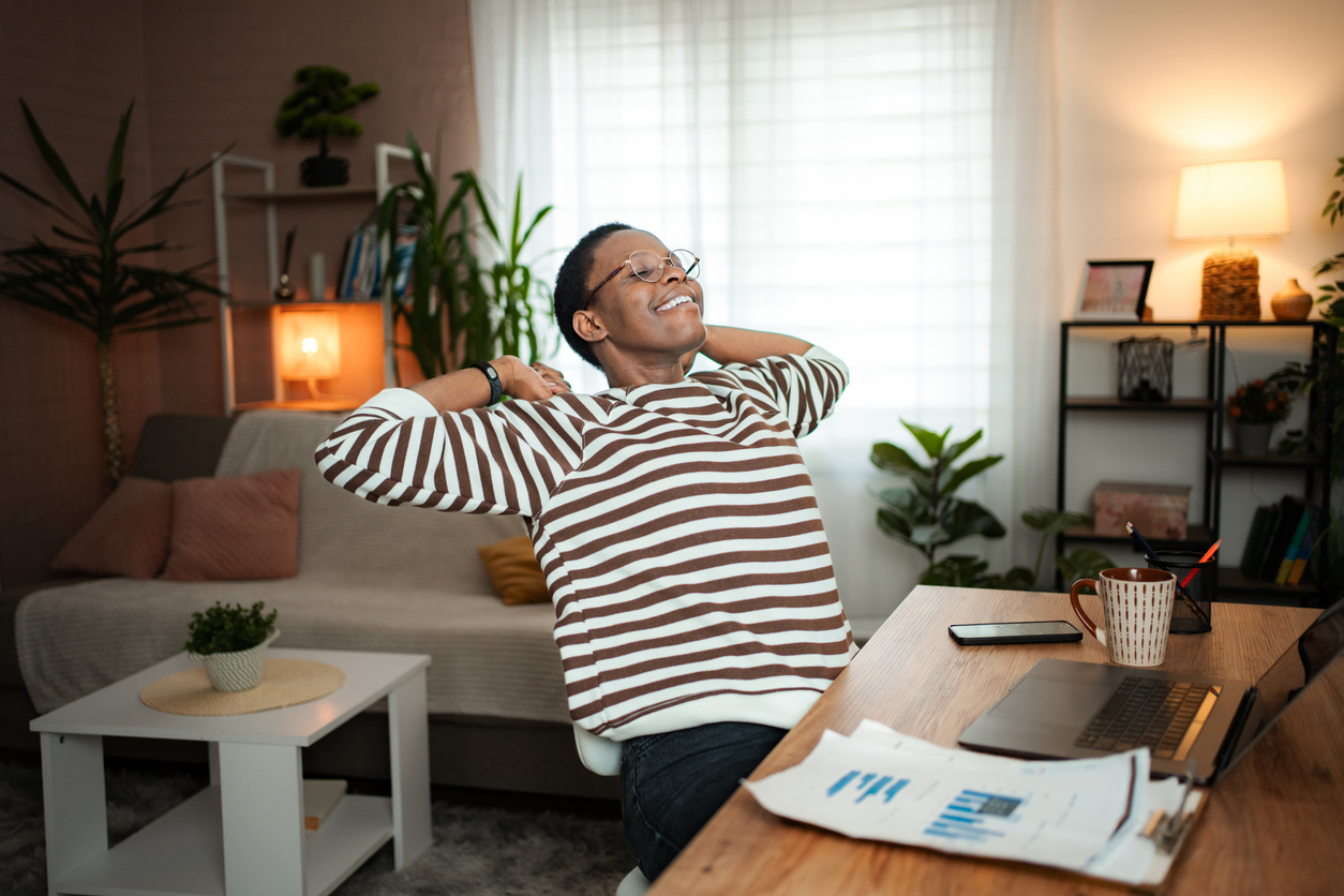 A man smiles and leans back at the end of a day working from home in his apartment.