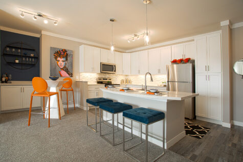 Open-concept kitchen at Allure in Centerville, Ohio by Hills Properties featuring white shaker cabinetry, stainless steel appliances, oversized island seating, quartz countertops, and modern pendant lighting.