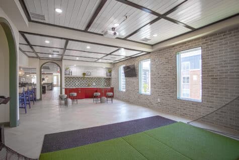Indoor golf simulator lounge with putting turf, bar seating, and contemporary clubhouse design at Relay 129 by HILLS Properties in Liberty Township, Ohio.